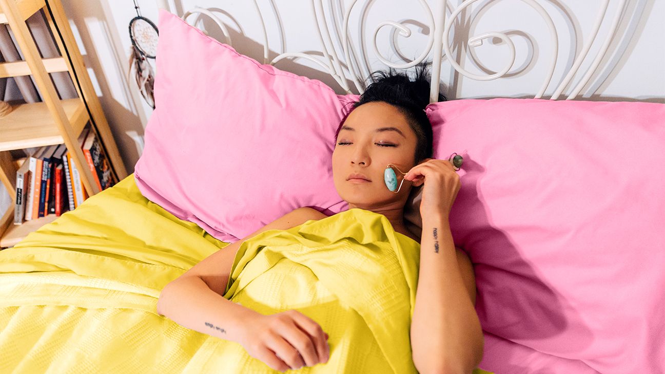 Young woman use jade roller on bed