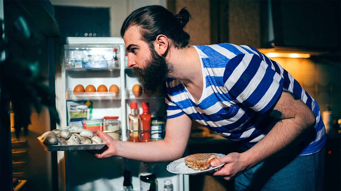 Young bearded man eating late night in the kitchen header