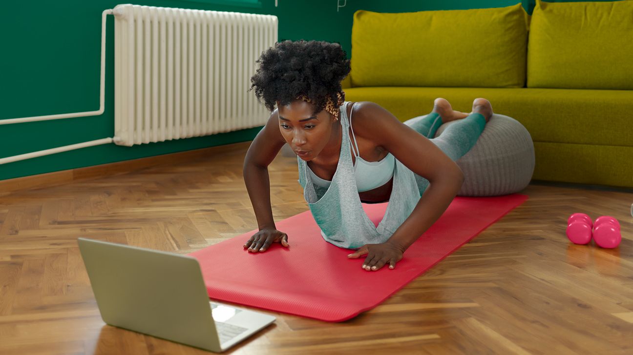 Young woman lying on stomach following exercises on her laptop