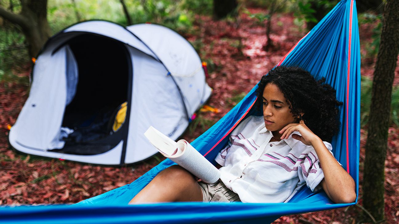 woman reading a book while lying in a hammock outdoors
