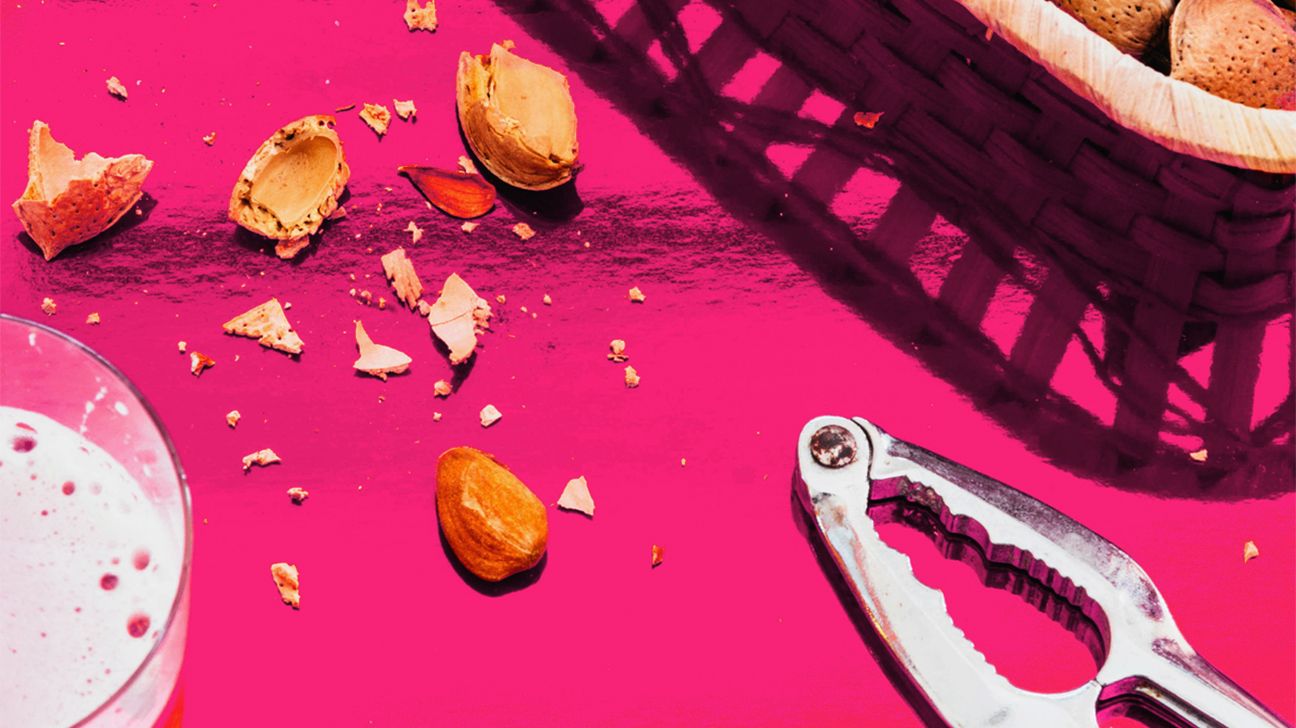 basket almonds with nut cracker on pink background