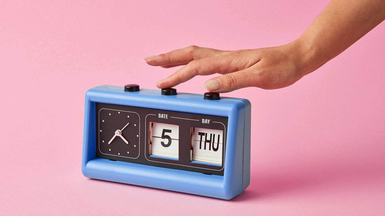 person pressing button on blue alarm clock
