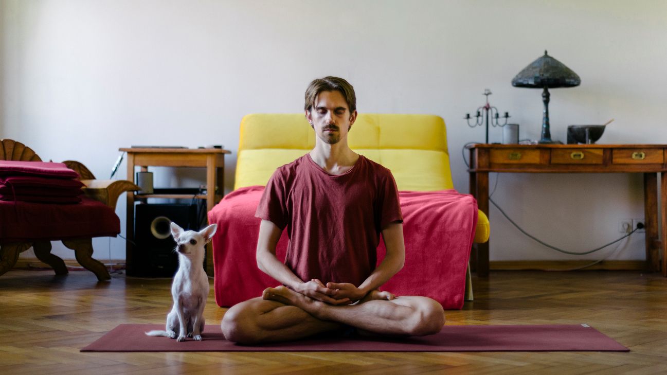 person meditating on floor next to small white dog