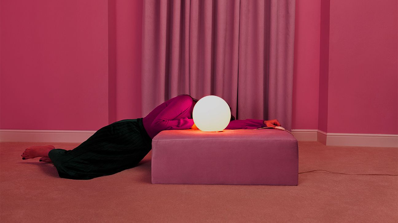 person laying on ottoman in pink room with lamp over face