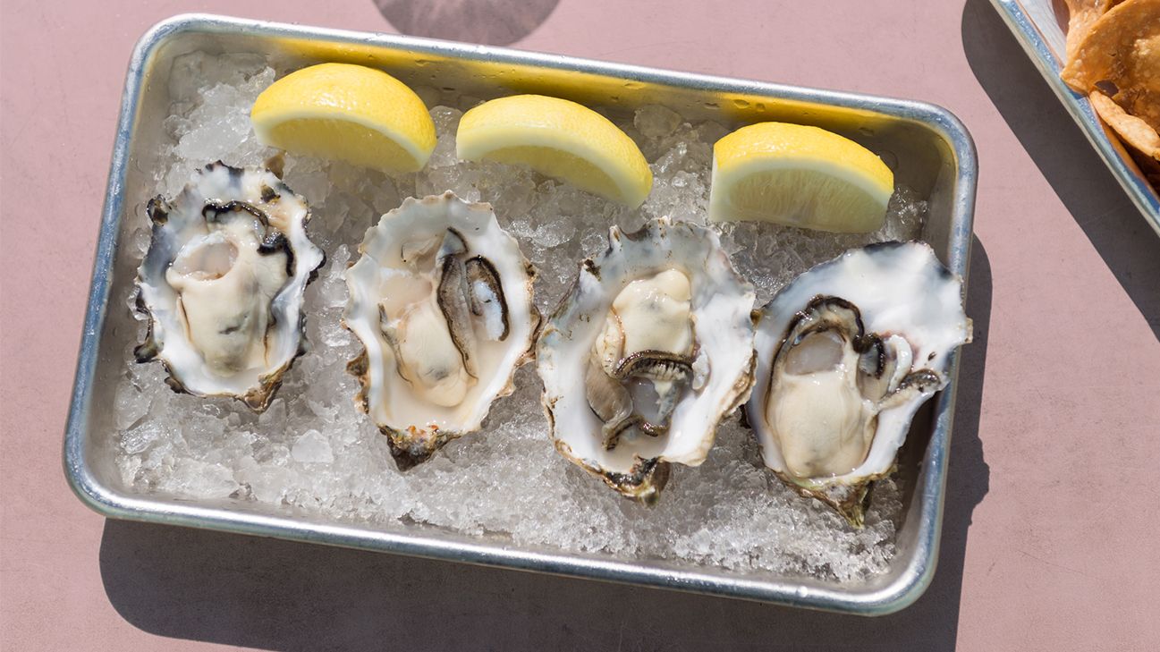 tray of oysters on ice with lemon wedges
