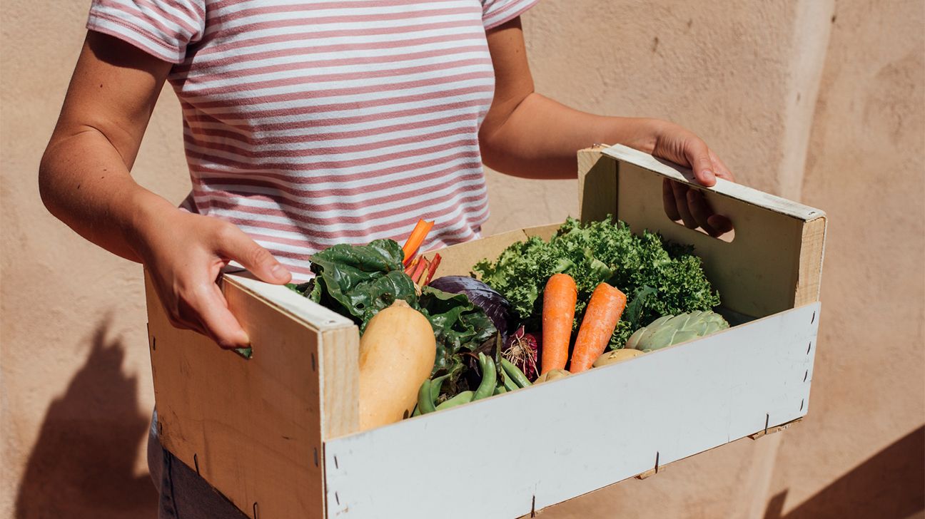 person holding a box of veggies with carrots