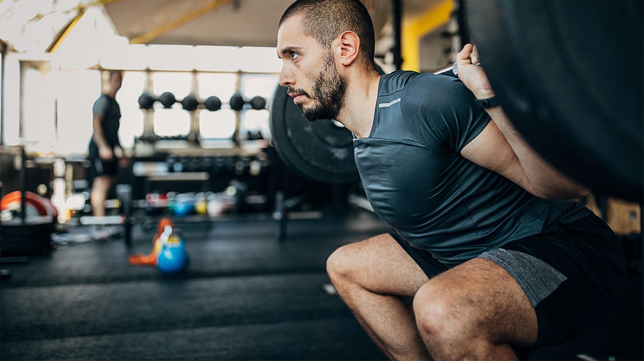 A person doing a barbell squat in a gym