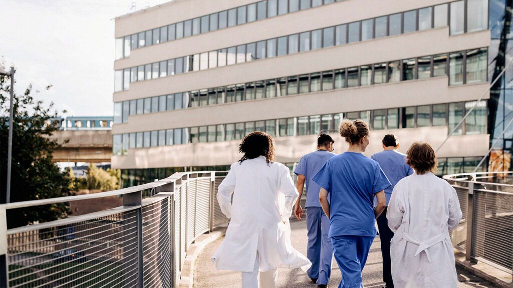Male and female healthcare professional walking on bridge leading towards hospital to make a prognosis