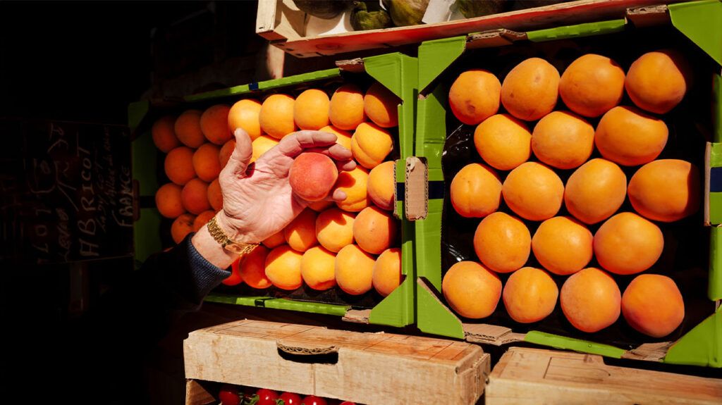 a hand picking up an apricot from a crate of fruit