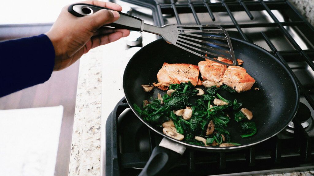 Woman Cooks Salmon With Spinach and Mushrooms as a way of adding vegetables into a keto diet