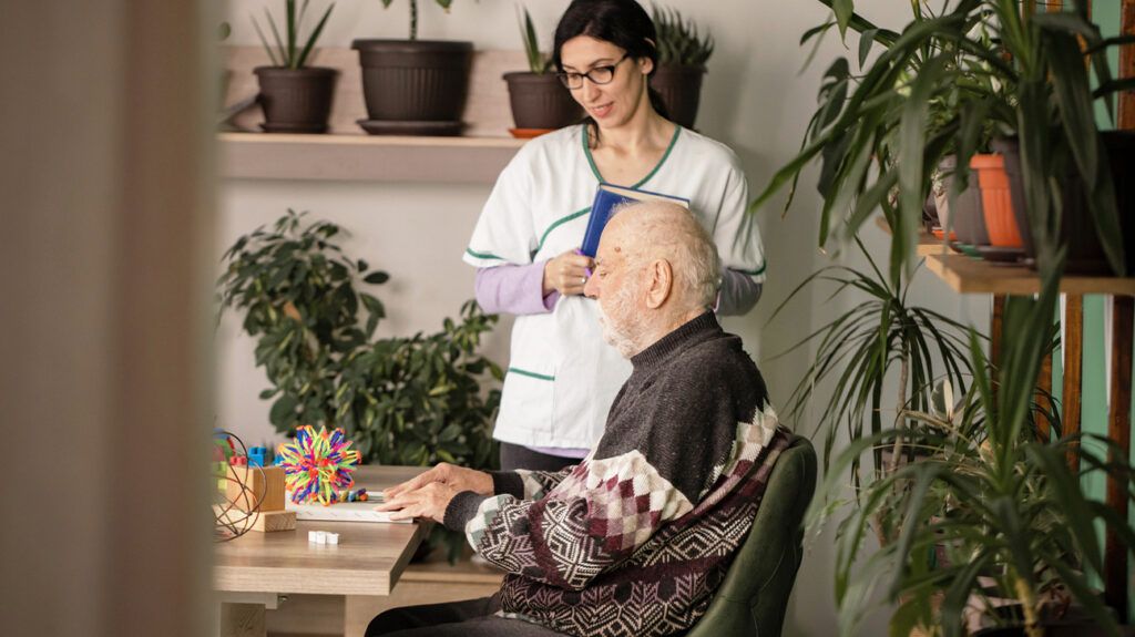 A nurse watching an older man with dementia use toys at a table in his home.