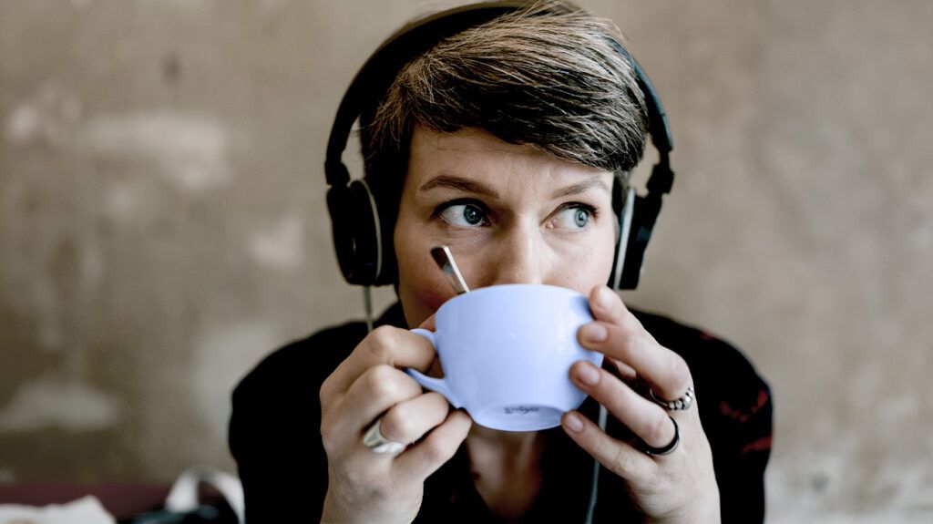 A person looks to the side while drinking a cup of coffee and listening to music with headphones