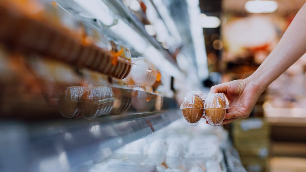 Someone grabbing a carton of eggs from a supermarket shelf