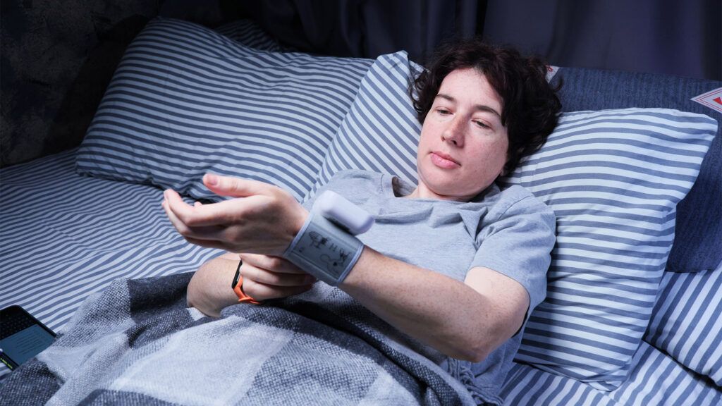A woman in bed measuring her blood pressure while lying down.