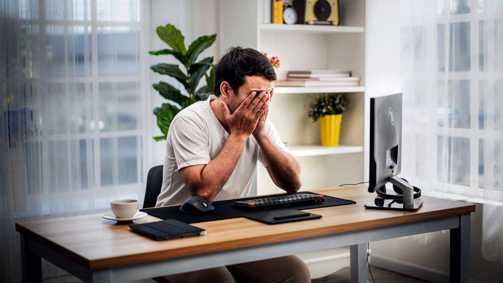 A person is sitting at a desk with their head in their hands.