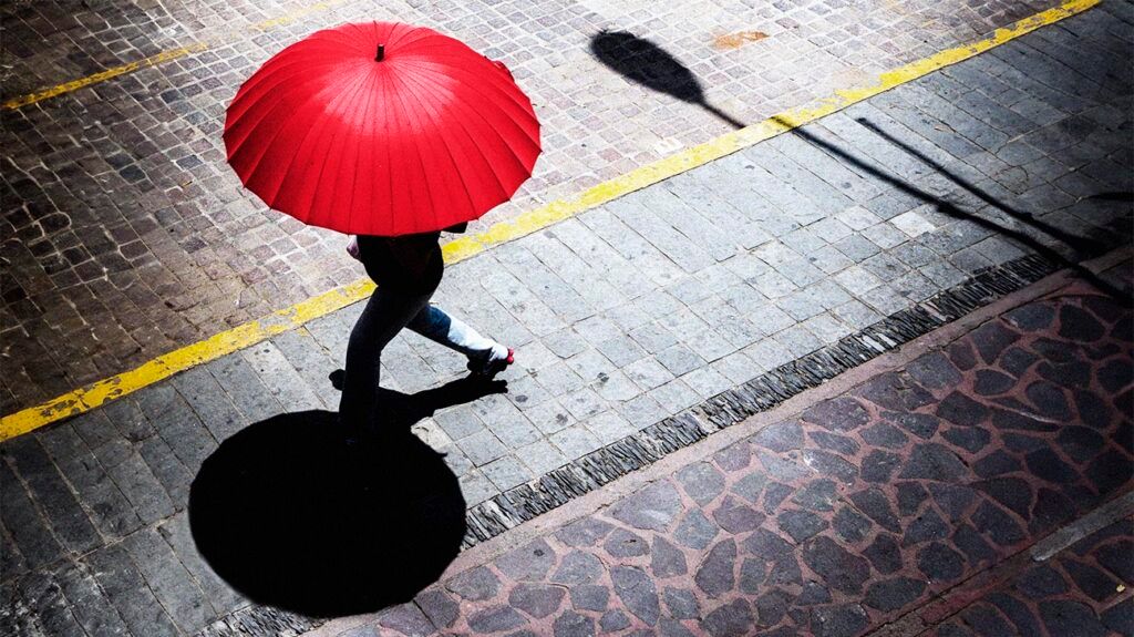 A person walking on a hot street under a red umbrella
