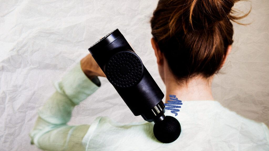 Rear view of a woman using a massage gun for tight neck muscles.