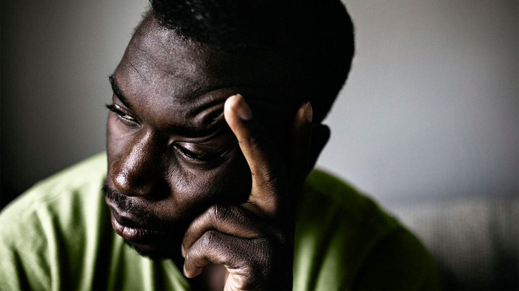 Close-up of a man holding his head in one hand while looking away.