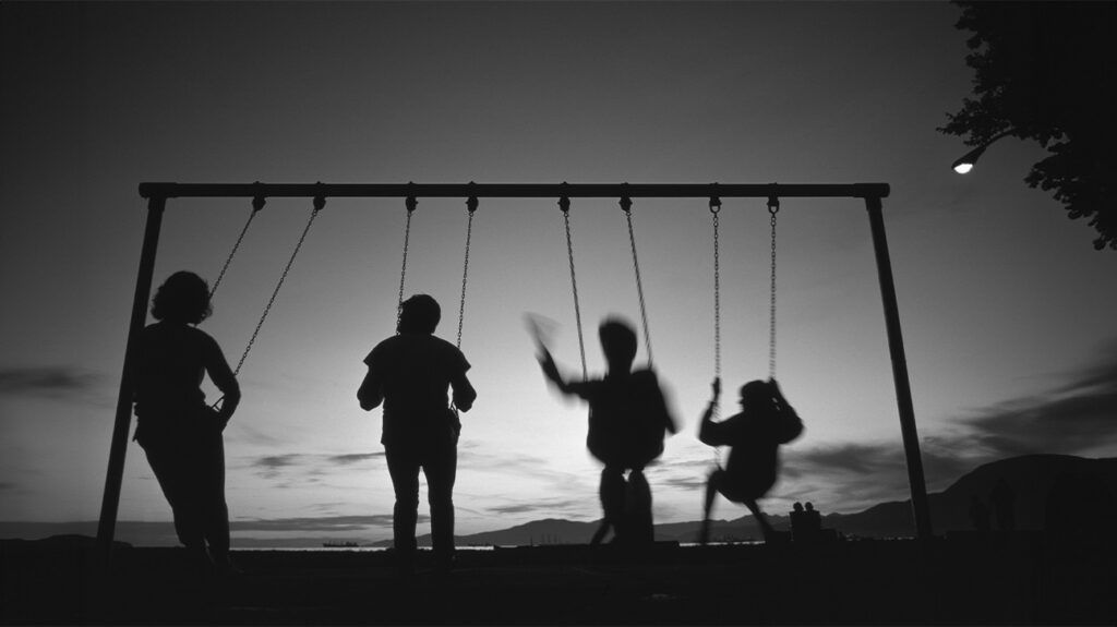 Silhouettes of children playing on a swing.