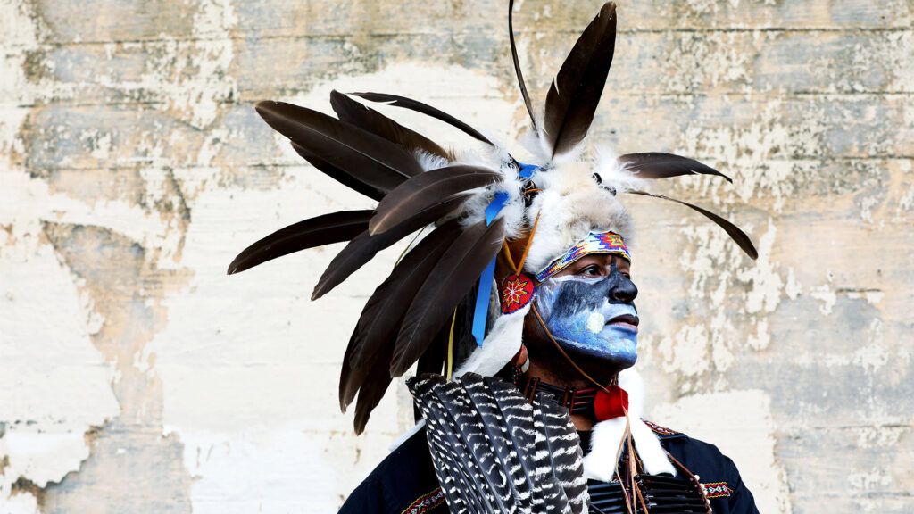 a two spirit person is wearing traditional face paint and a headdress