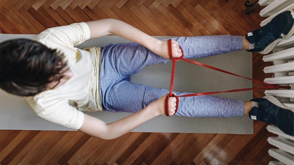A boy exercising with a strap at home.