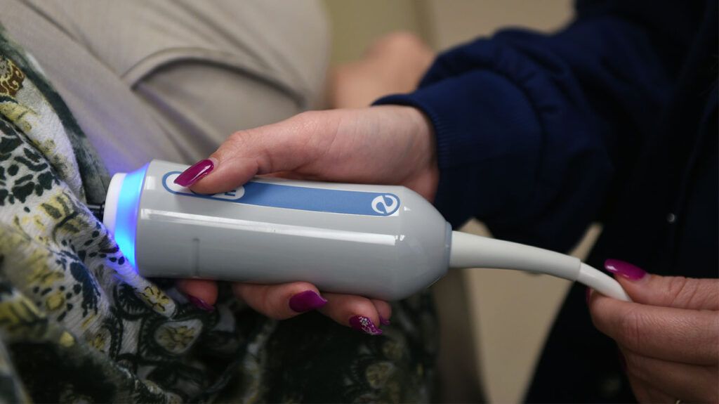 Close-up of a person holding a FibroScan device against a person's abdomen.
