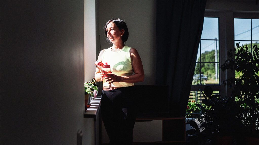 A woman holding a water bottle in gym clothes while looking out of a window.