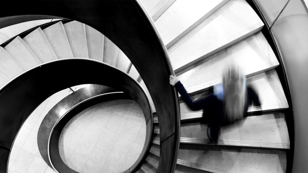 A blurred person ascending a spiral staircase.