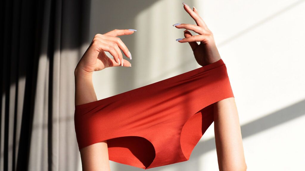 Red underwear that a person is holding overhead, with an arm in each leg hole.