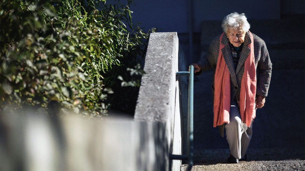 An older woman with dementia walking up steps outside.