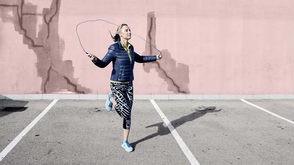 a woman is skipping outside with a pink wall in the background