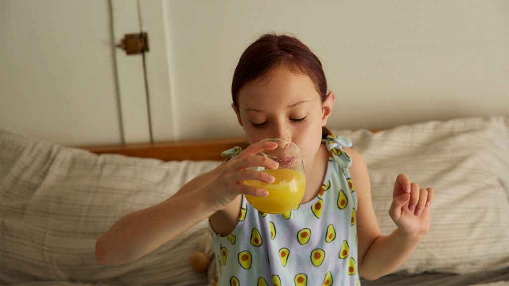 A young girl drinking a glass of orange juice.