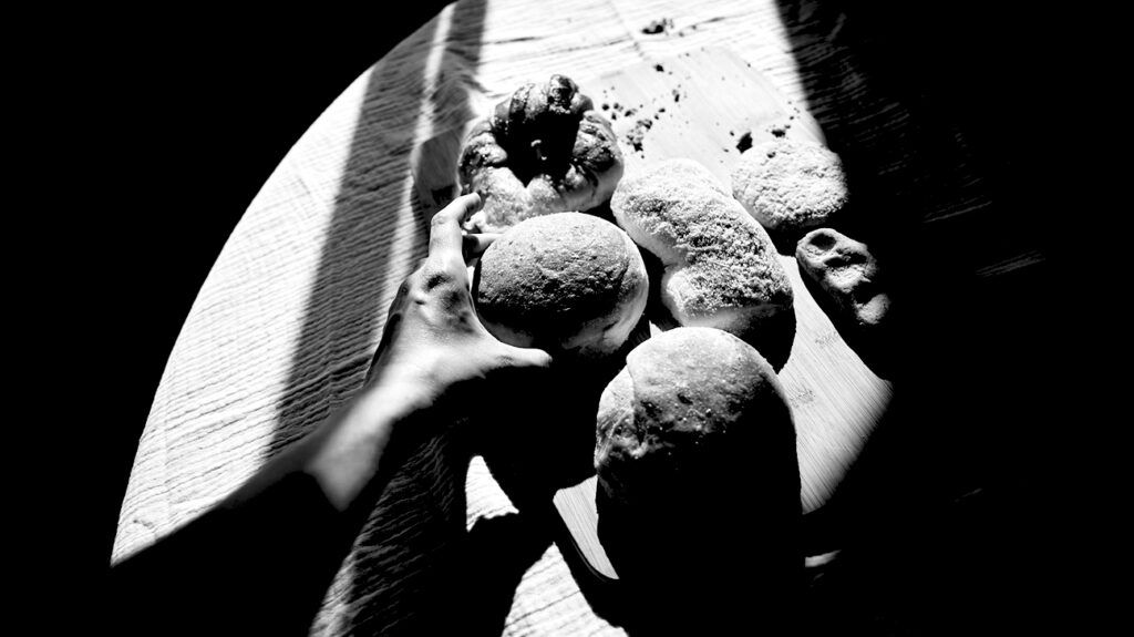 A person's hand reaching for bread rolls on a table. -2