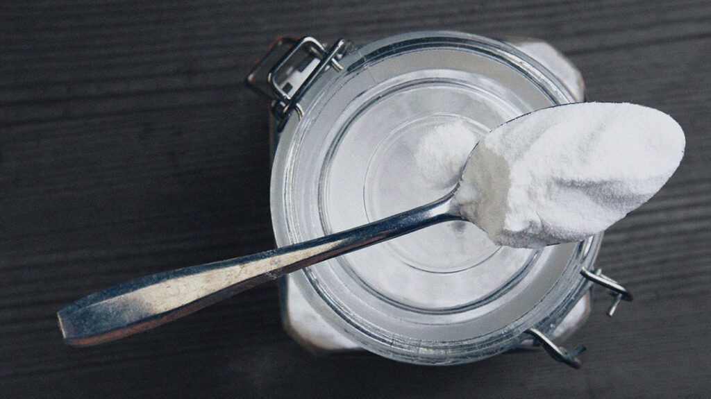 A spoon with baking soda sat over a glass jar of baking soda