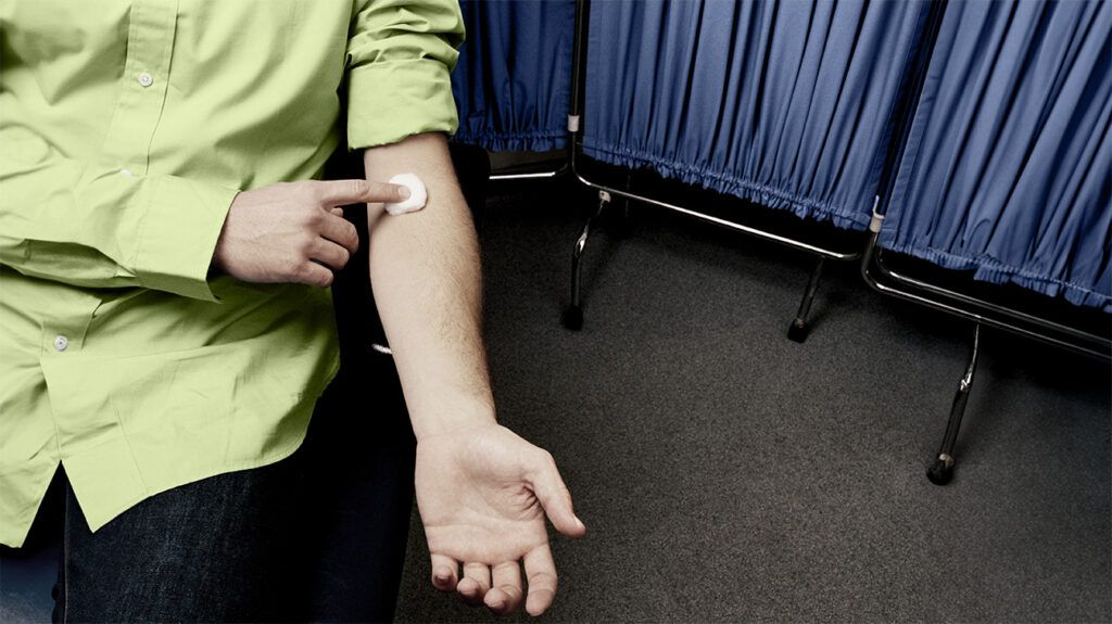 A person holds a piece of cotton on their inner arm after a blood test, keeping it pressed to stop the bleeding