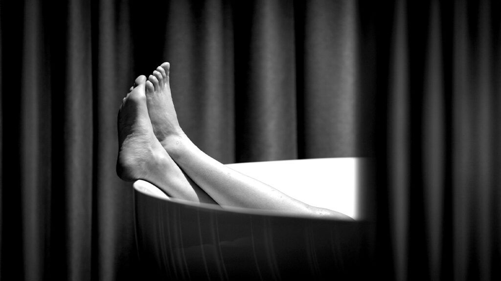 Black and white image, a person's feet sticking out of the end of a bath.