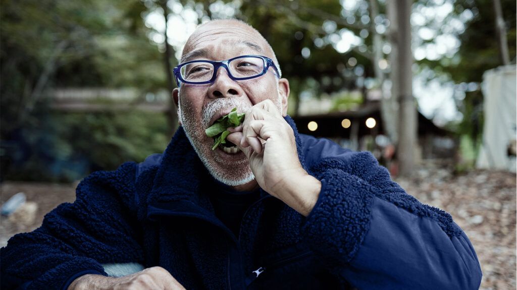 uomo asiatico più anziano con gli occhiali che mangia verdure verdi