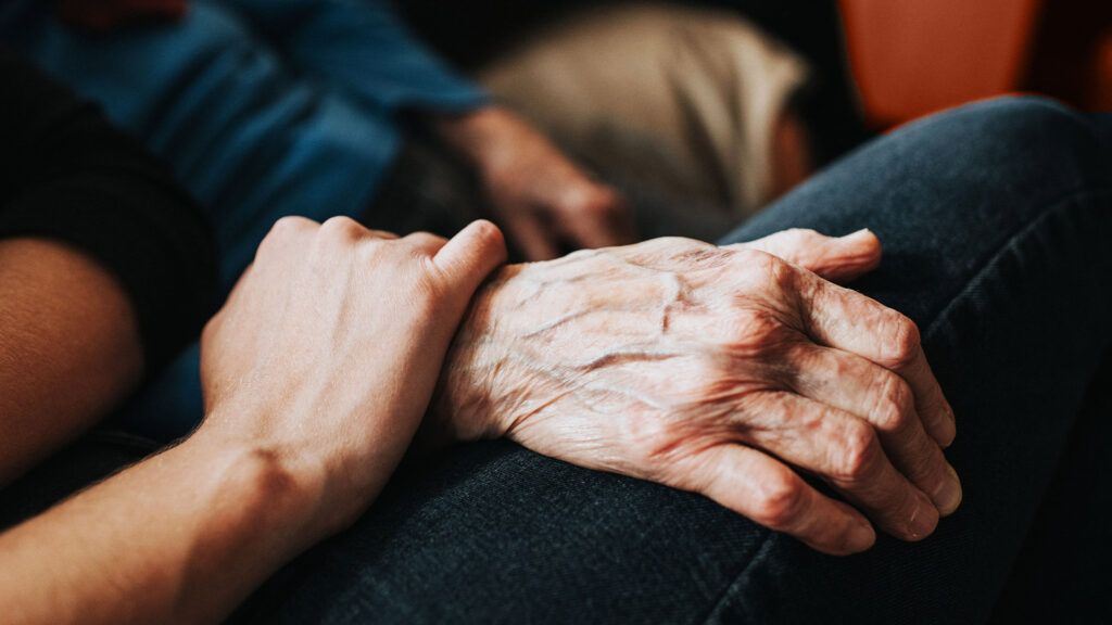 A person holding the back of an elderly person's hand