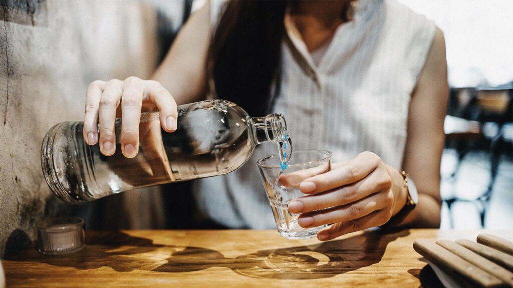 Midsection of young Asian woman pouring water from bottle into the glass in a restaurant