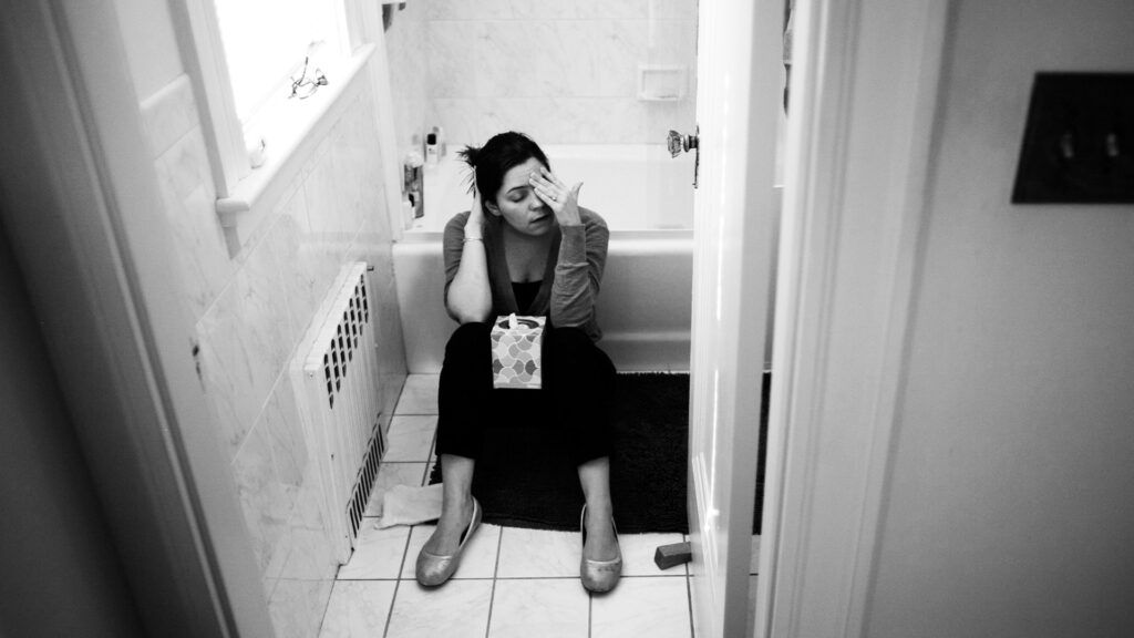 Female sitting on the bathroom floor with her head in her hands