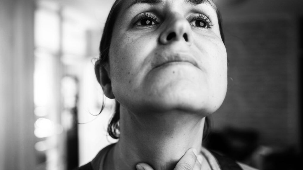 Black & white image of a female feeling the front of her neck