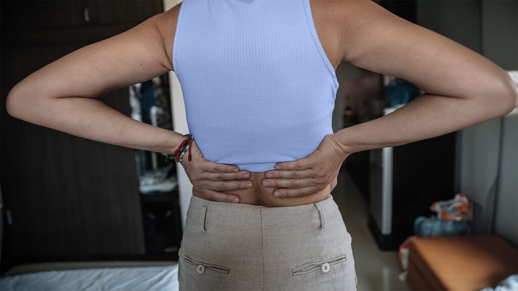 A person placing their hands on their lower back, near the kidneys -1.