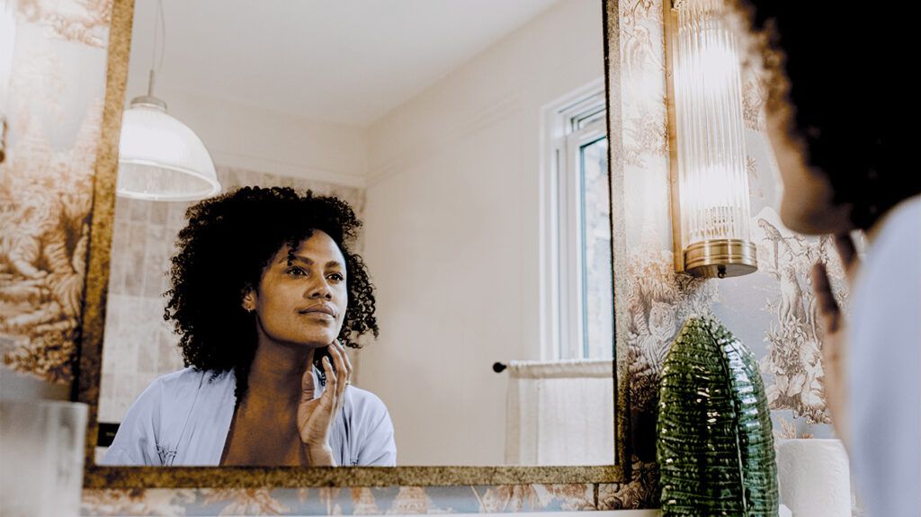 A woman looking a mirror touching her neck inquisitively.