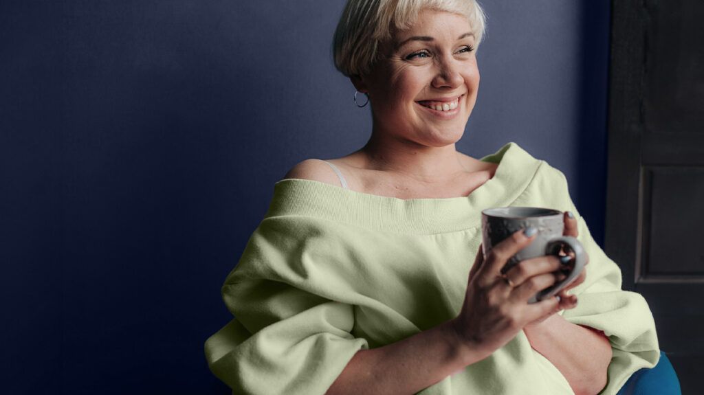 A woman holding a cup of herbal tea and smiling.