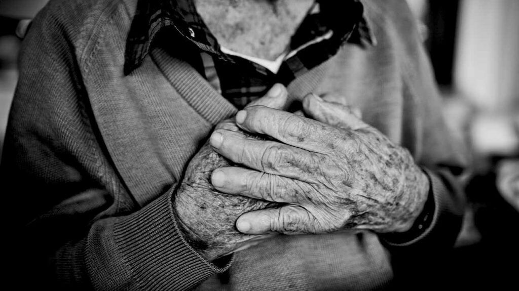 Black and white image of an older person's hands covering their heart