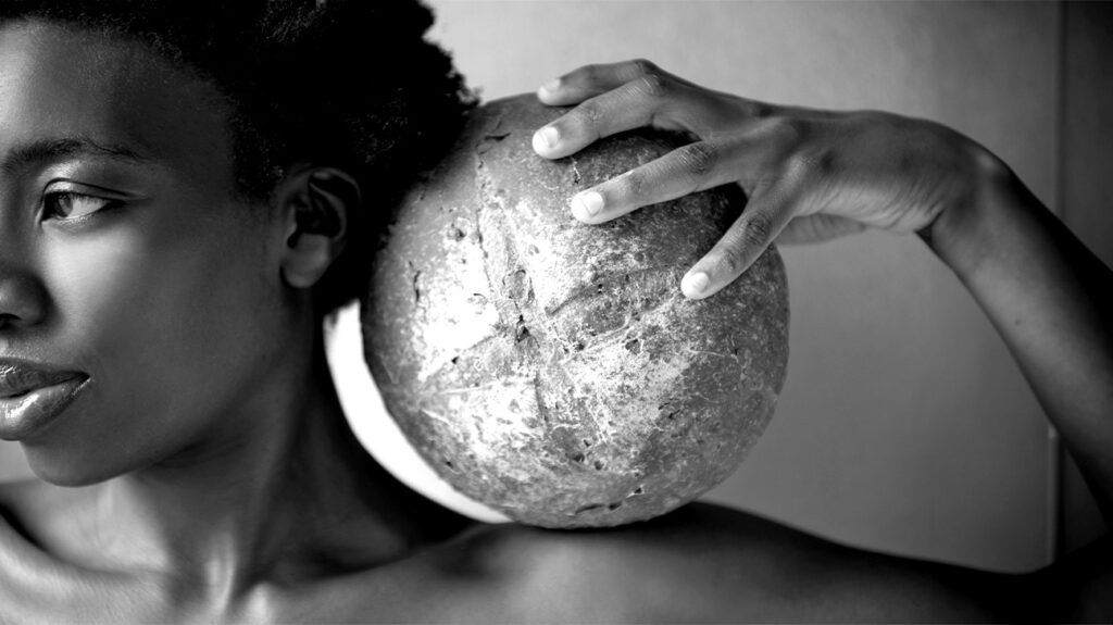 A woman holds a round loaf of wholegrain bread on her shoulder