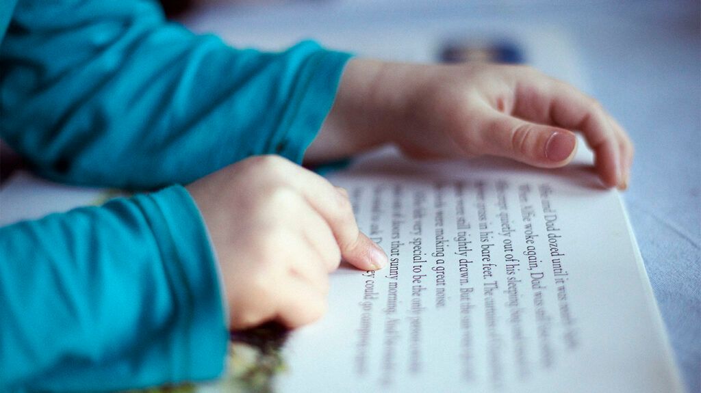 a close up photo of a young child's fingers pointing at text in a book