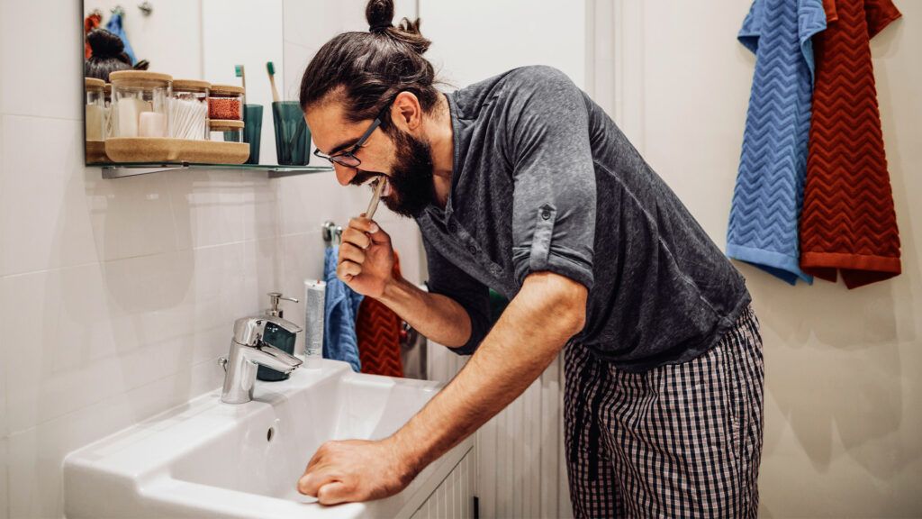Un uomo si lava i denti nel lavandino del bagno