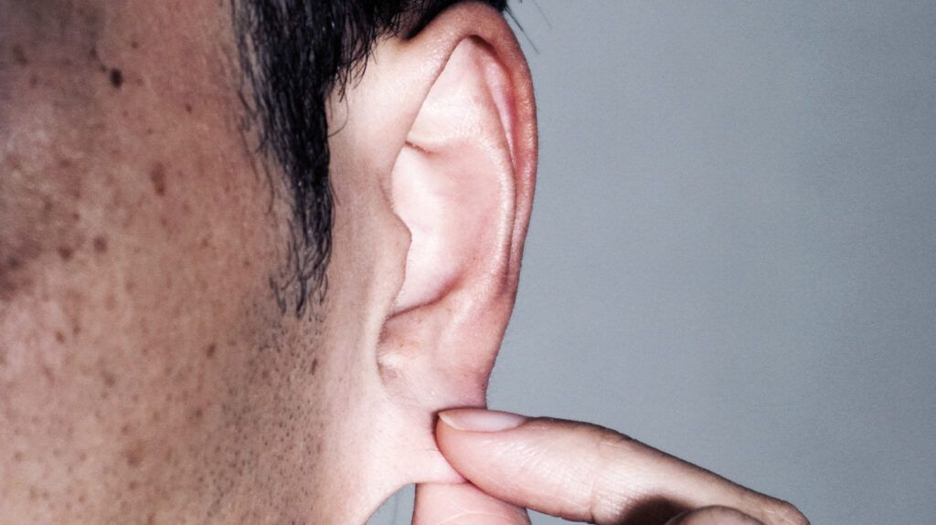Close-up shot of a man touching his earlobe.