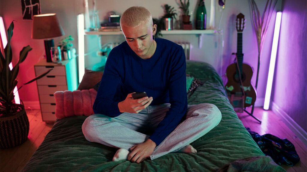 Young man sitting on a bed looking at a phone